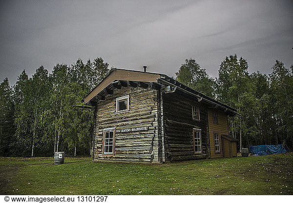 Slaven's roadhouse on field by trees at Yukon_Charley Rivers National Preserve against cloudy sky