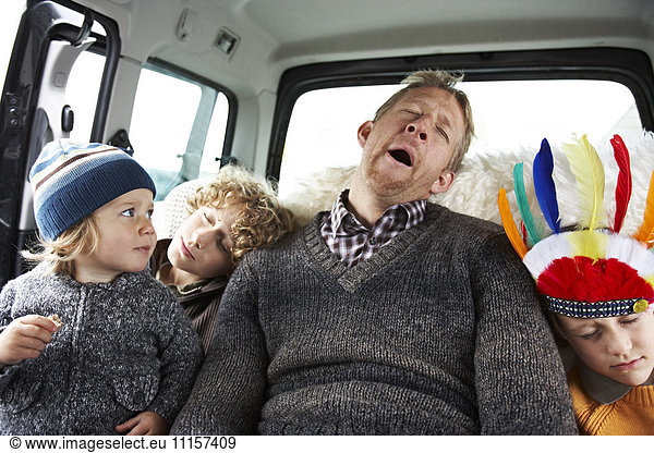 Sleeping father sitting in car on back seat with his sons