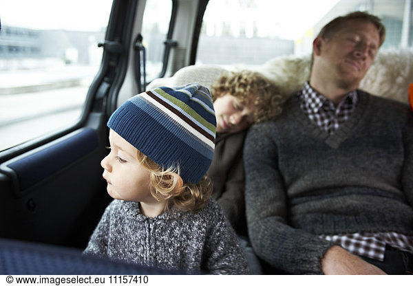 Sleeping father sitting in car on back seat with his sons