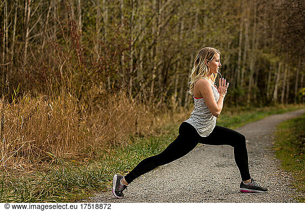Slender woman in thirties holds yoga pose on trail