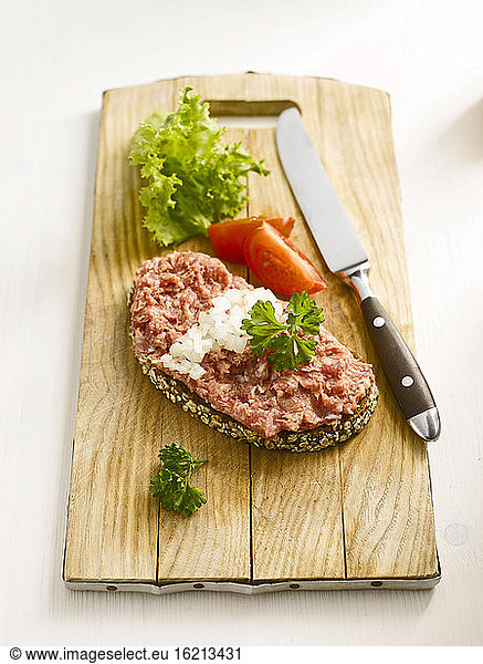 Slice of bread with minced meat and knife on chopping board  close-up