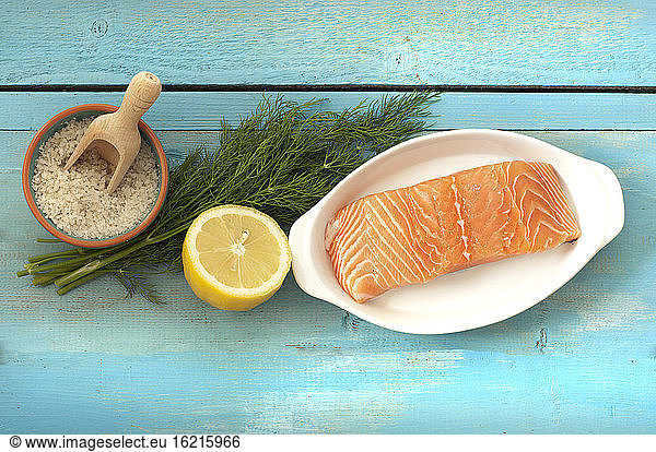 Slice of salmon with lemon  dill and salt on wooden table  close up