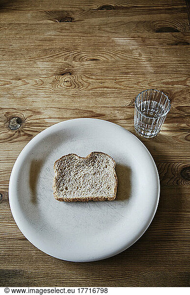 Slice Of Stale Bread On A White Plate With A Glass Of Water