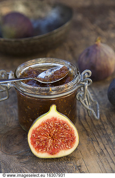 Sliced fig  whole figs (Ficus carica) and a glass of fig jam on wooden table  studio shot