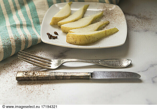 Sliced Pear on White Plate with Antique Silverware on Marble