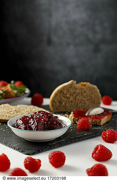 Slices of bread  fresh raspberries and bowl of raspberry jam