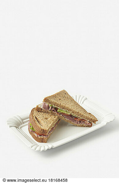 Slices of brown bread ham sandwich on tray against white background