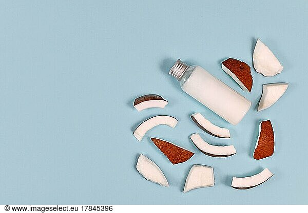 Slices of coconut fruit and bottle filled with coconut oil used for food preparation and cosmetic beauty products on blue background with copy space