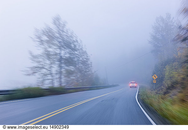 Slow shutter speed exposure of a car driving down a foggy road  South-central Alaska; Palmer  Alaska  United States of America