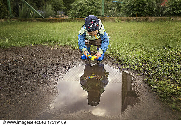 Smal boy in blue wellies taking photo of his own reflection in p