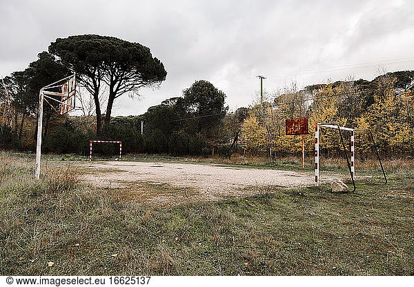 Small abandoned sports field with goals and basketball hoops