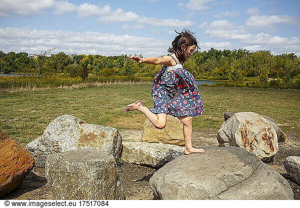 Small barefoot child in sundress leaps between large rocks