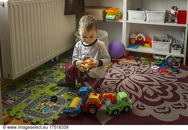 Small blonde boy in his room sitting on the floor and playing wi