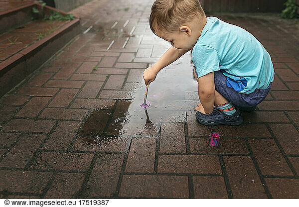 Small blonde boy painting pavement with brush and pink paint