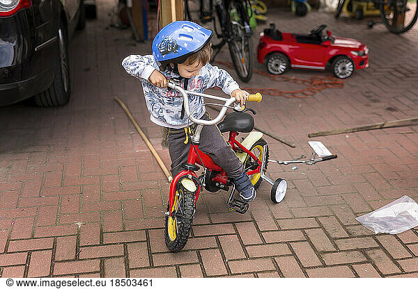 Small boy trying to get up on bike with side wheels