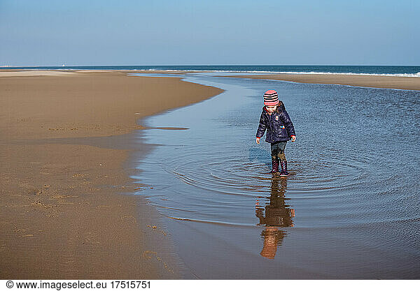 Small child makes ripples in water at beach on sunny winter day