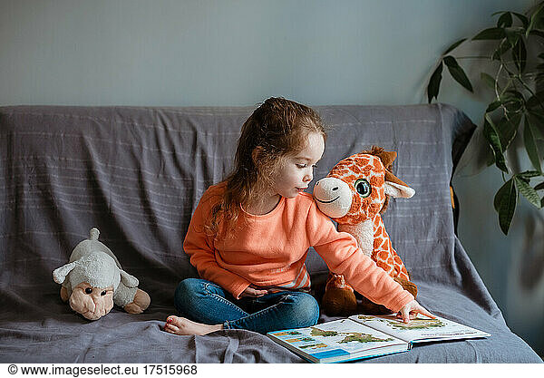 Small child reads to toys from books on sofa