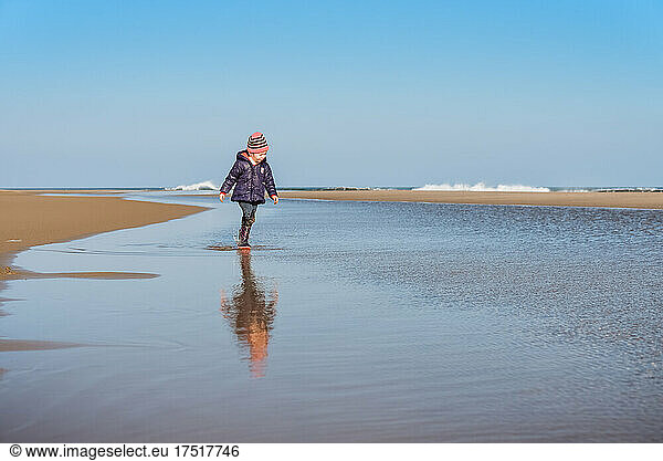 Small child walks in water at beach on sunny day in winter
