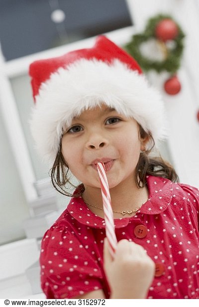 Small girl in Father Christmas hat eating candy cane