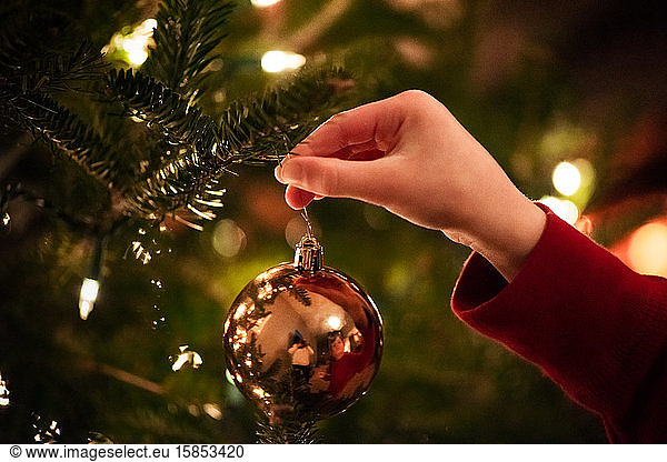 small hand placing a ornament onto a Christmas tree