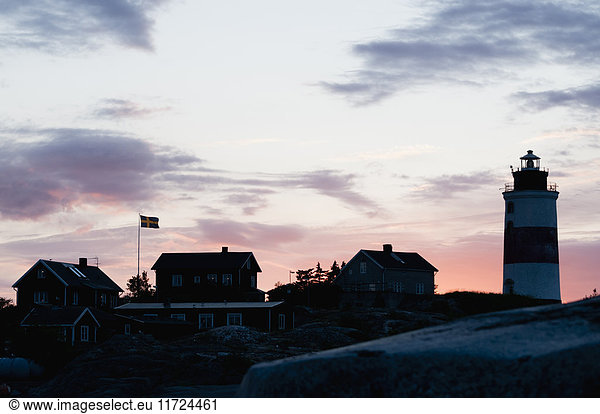 Small houses and lighthouse by sea at sunset