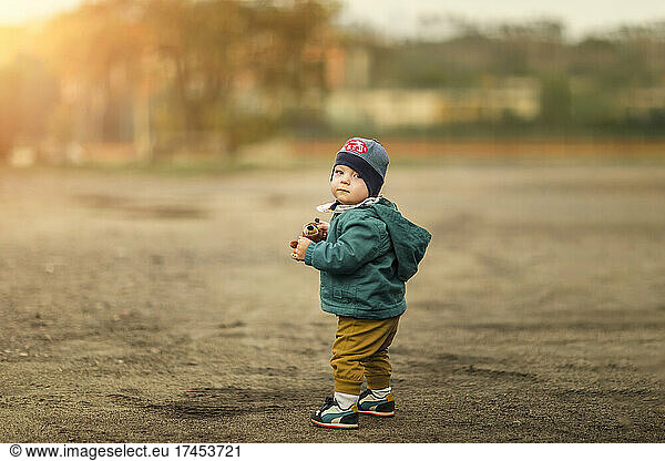Small infant boy standing on the ground and holding small stuffe