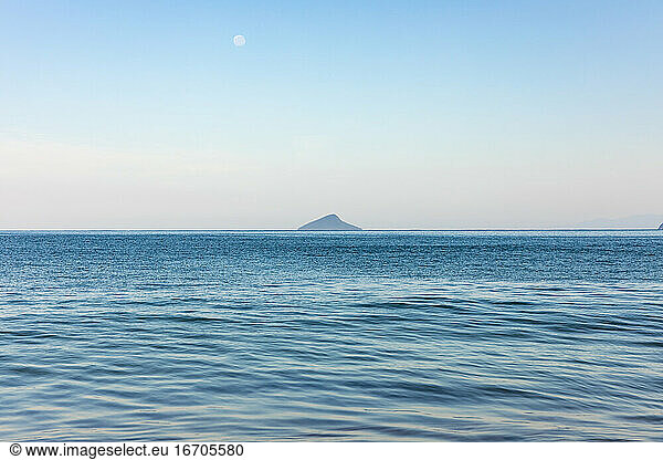 Small island with full moon in bright summer day