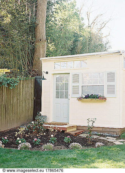 Small ivory shed with blue shutters and garden