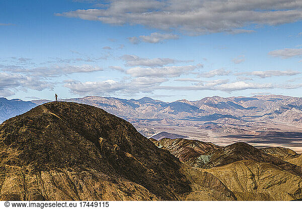 small tiny lone person stands on peak in vastness of Death Valley.