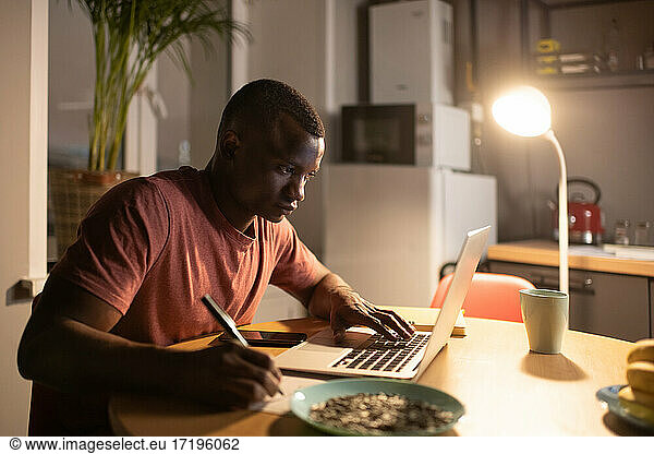 Smart black man using laptop and making notes