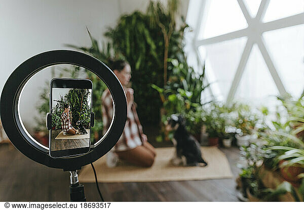Smart phone mounted on ring light filming woman vlogging with dog at home