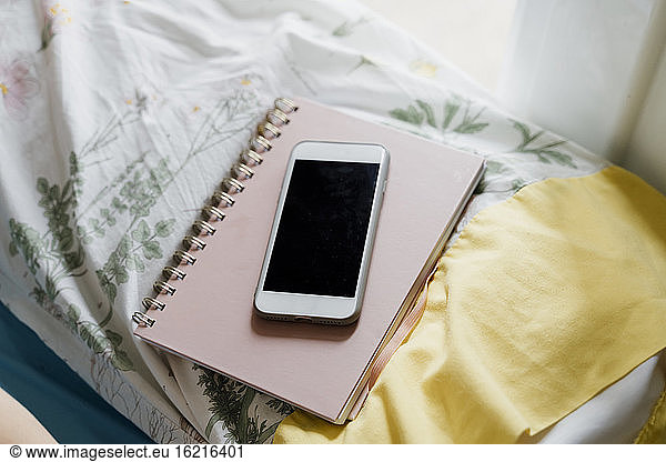 Smartphone auf Notizblock über dem Kopfkissen im Schlafzimmer