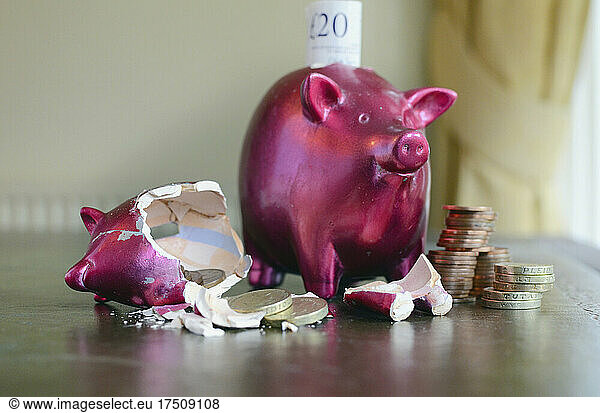 Smashed and whole piggy bank with piles of pounds on table and notes  concept of saving and spending money.