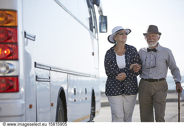 Smiling active senior couple tourists walking along bus