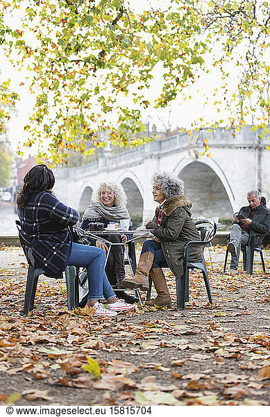 Smiling active senior women friends enjoying coffee at autumn park cafe