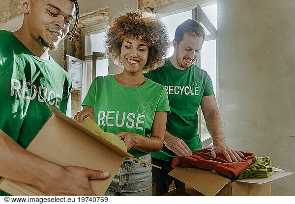 Smiling activists putting secondhand clothes in cardboard boxes