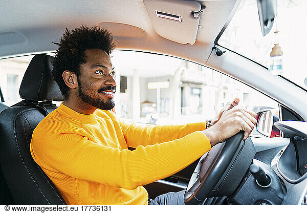 Smiling Afro man wearing yellow t-shirt driving car