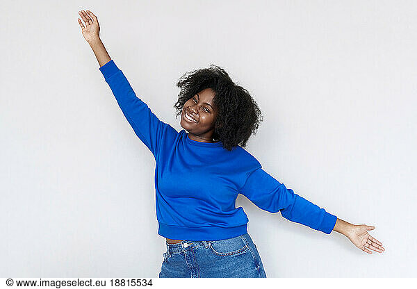 Smiling Afro woman with arms outstretched standing against white background