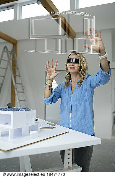 Smiling architect wearing virtual reality simulator examining house model over table