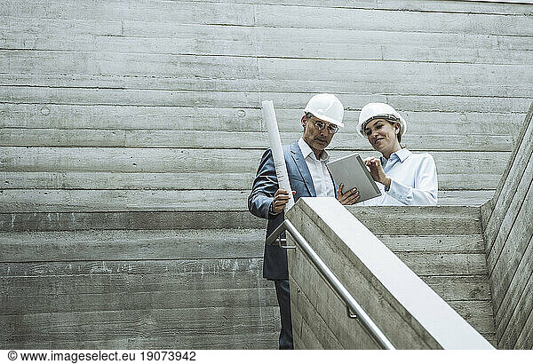 Smiling architects having discussion over tablet PC on staircase