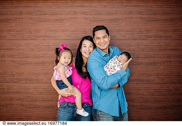 Smiling Asian-American family with young daughter and newborn baby