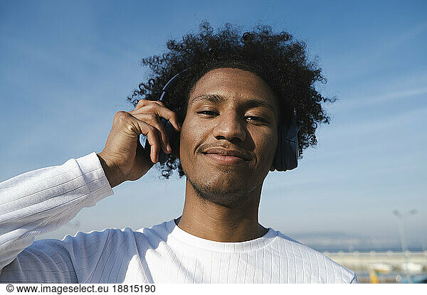 Smiling athlete holding wireless headphones at sunny day