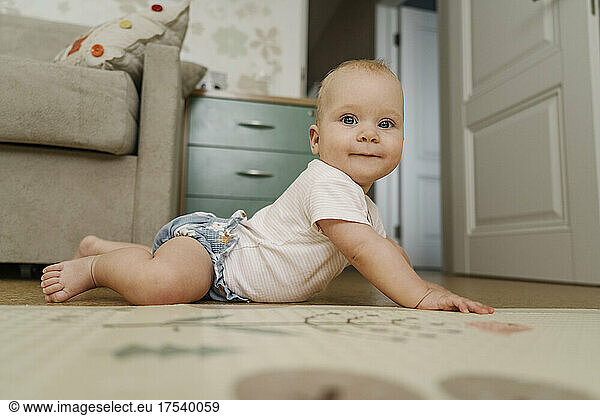 Smiling baby girl lying on floor at home