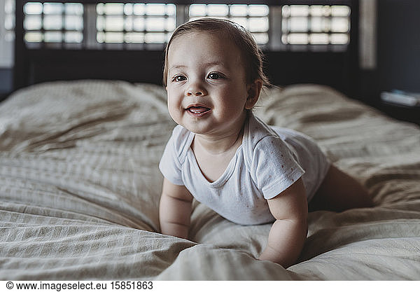 Smiling baby with two teeth crawling on bed in light from window