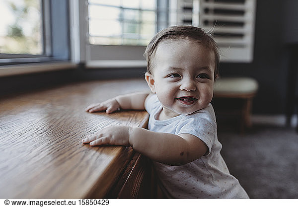 Smiling baby with two teeth standing by window seat