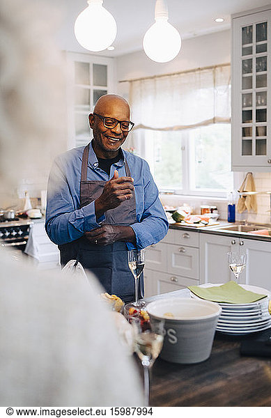 Smiling bald senior man rolling up sleeves before preparing dinner in kitchen at home