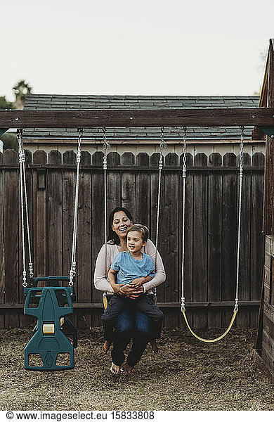 Smiling barefoot mom and 5 yr old son on backyard swing