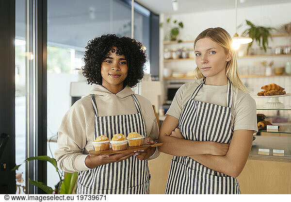 Smiling barista holding cupcakes with colleague in coffee shop