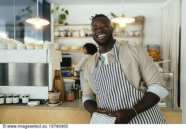 Smiling barista wearing apron holding towel in coffee shop