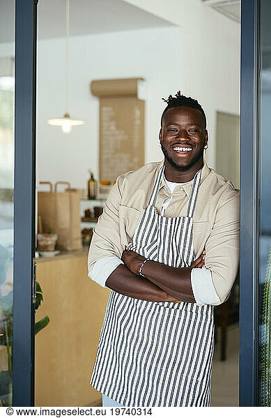 Smiling barista with arms crossed leaning on door of coffee shop
